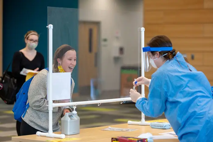A student getting tested at SUNY Adirondack, with a plexiglass barrier between her and the tester